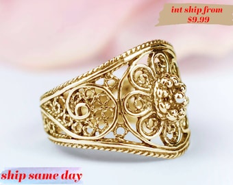 May include: A gold filigree ring with a floral design. The ring is wide and has a delicate, intricate pattern.