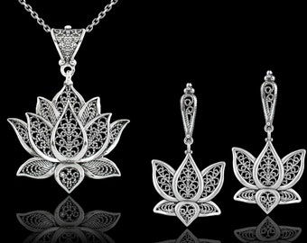 May include: A silver lotus flower pendant necklace and matching earrings. The pendant and earrings are made of intricate filigree work and have a delicate, feminine design.
