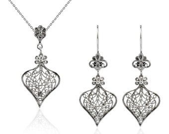May include: A silver filigree necklace and earrings set. The necklace has a delicate chain and a pendant with a floral design. The earrings are drop earrings with a similar floral design.