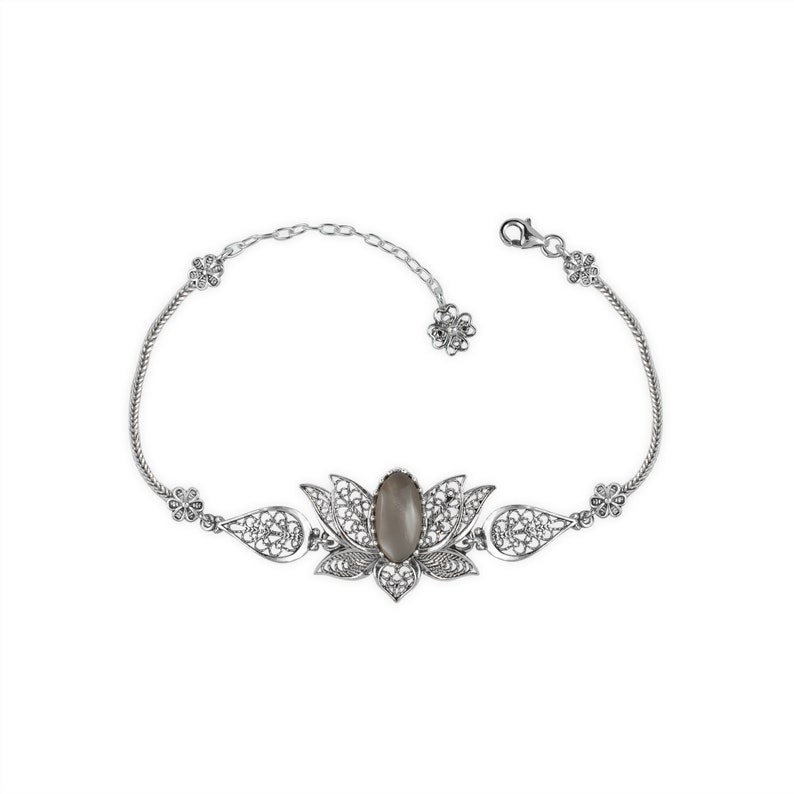 May include: A silver bracelet with a filigree design featuring a gray stone in the center. The bracelet is shaped like a lotus flower.