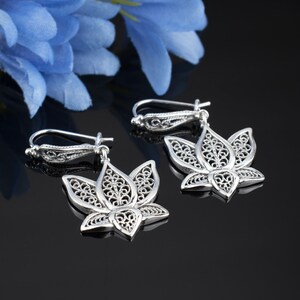 May include: A pair of silver filigree earrings shaped like lotus flowers. The earrings are delicate and intricate, with a floral design.