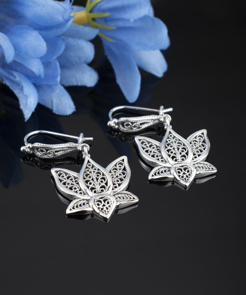 May include: A pair of silver filigree earrings shaped like lotus flowers. The earrings are delicate and intricate, with a floral design.