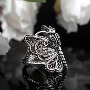 May include: A silver filigree butterfly ring. The ring is made of delicate, intricate metalwork and features a butterfly design with openwork wings.