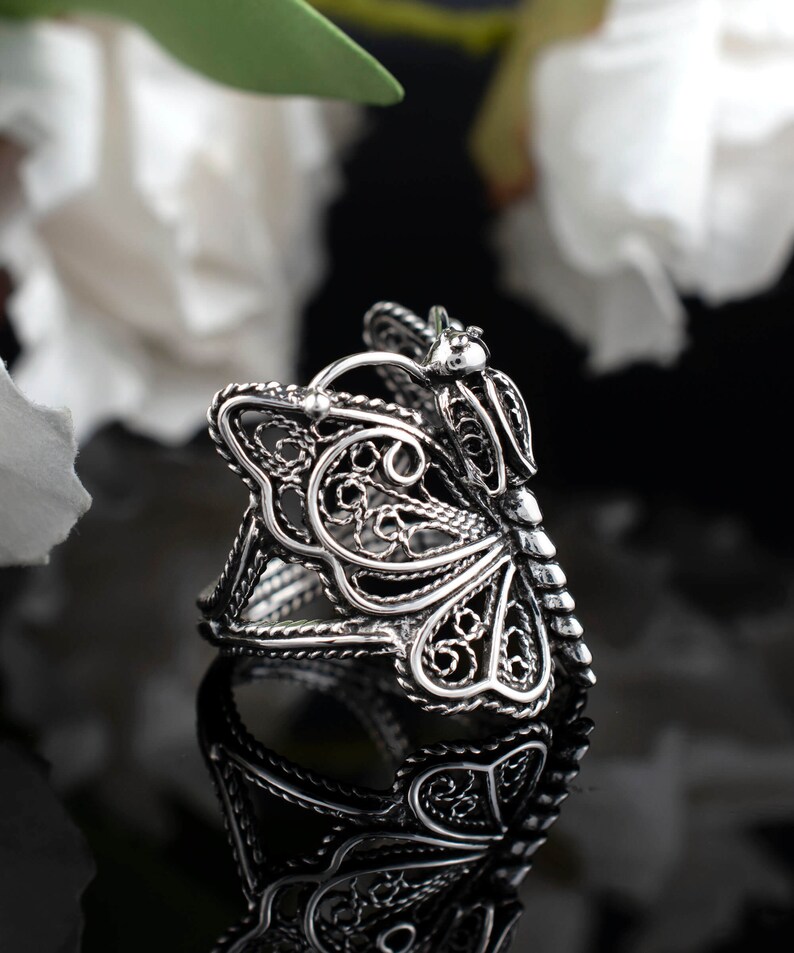 May include: A silver filigree butterfly ring. The ring is made of delicate, intricate metalwork and features a butterfly design with openwork wings.