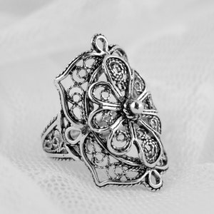 May include: A silver filigree ring with a floral design. The ring is delicate and intricate, with a small bead at the center of the flower.