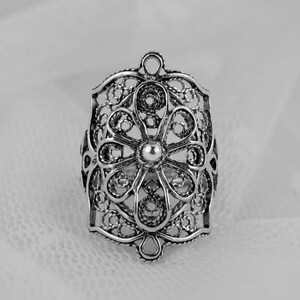 May include: A silver filigree ring with a floral design. The ring is intricate and delicate, with a small round center stone.