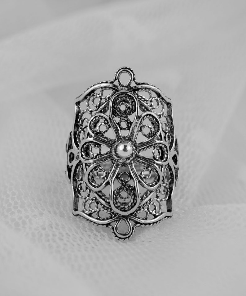 May include: A silver filigree ring with a floral design. The ring is intricate and delicate, with a small round center stone.