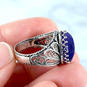May include: A silver filigree ring featuring a large oval lapis lazuli gemstone. The ring boasts a delicate, intricate design and is set with a deep blue stone.