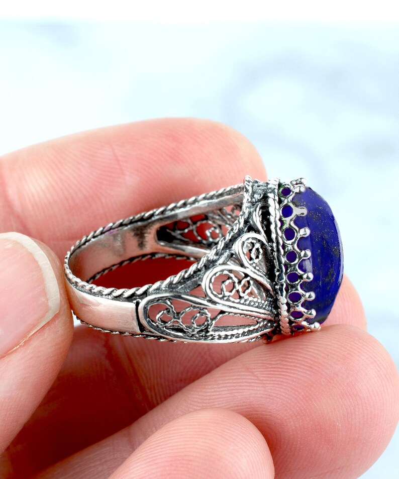 May include: A silver filigree ring featuring a large oval lapis lazuli gemstone. The ring boasts a delicate, intricate design and is set with a deep blue stone.