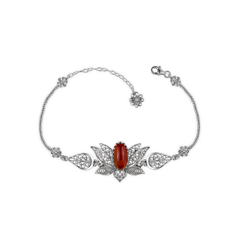 May include: A silver filigree bracelet with a red gemstone set in a lotus flower design.