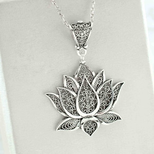 May include: A silver filigree lotus flower pendant necklace. The pendant is detailed and intricate, with a delicate design.
