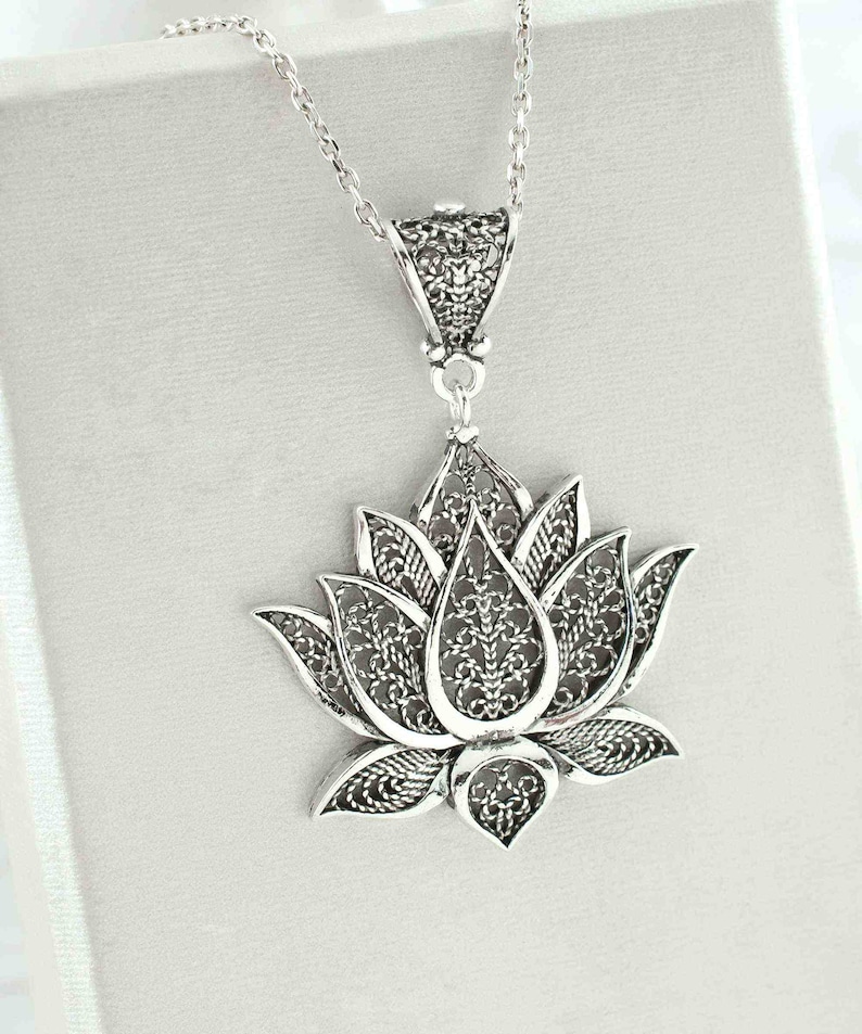 May include: A silver filigree lotus flower pendant necklace. The pendant is detailed and intricate, with a delicate design.