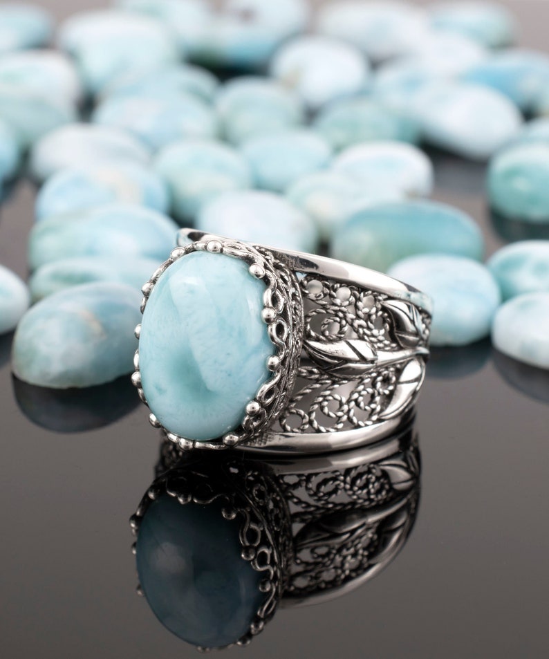 May include: A silver ring featuring a large oval blue gemstone set in a filigree design.