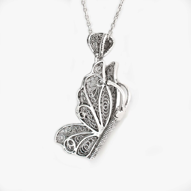 May include: A silver filigree butterfly pendant necklace. The butterfly is detailed and intricate, with a delicate chain.