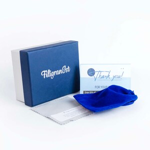 May include: A blue box with the text "FiligranIst" on it. A blue velvet pouch and a thank you card with the text "Thank you! For your purchase. Enjoy 20% off your next order." are in front of the box.