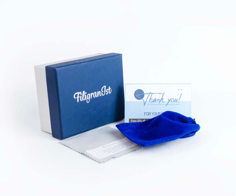 May include: A blue box with the text "FiligranIst" on it. A blue velvet pouch and a thank you card with the text "Thank you! For your purchase. Enjoy 20% off your next order." are in front of the box.