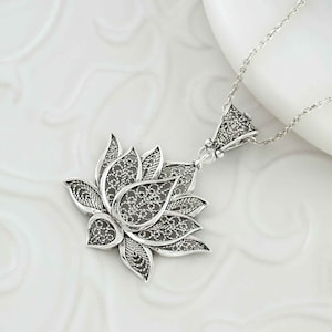 May include: A silver filigree lotus flower pendant necklace. The pendant is detailed and intricate, with a delicate design.