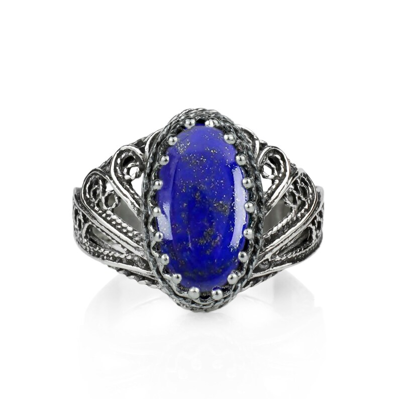 May include: A silver ring featuring an oval, deep blue gemstone with gold flecks. The gemstone is set in a detailed, filigree-style silver band. The ring has an ornate, vintage design.