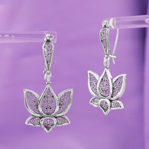 May include: A pair of silver filigree earrings with a lotus flower design. The earrings are hanging from a silver hook.