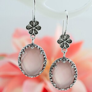 May include: Silver dangle earrings with a pink oval gemstone and a silver flower charm.
