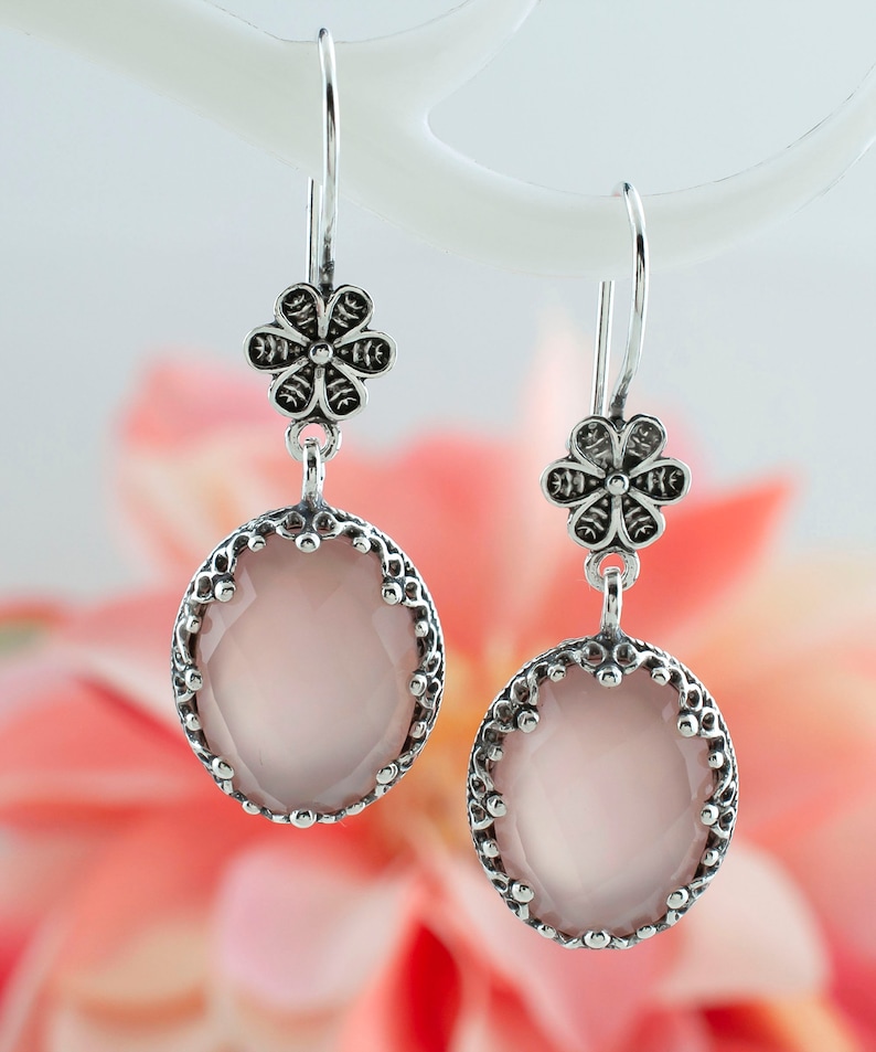 May include: Silver dangle earrings with a pink oval gemstone and a silver flower charm.