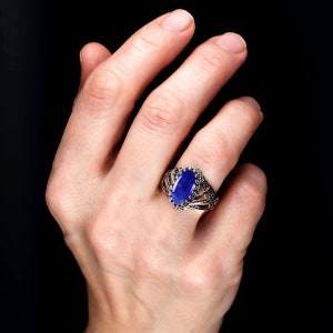 May include: A silver ring featuring a large, oval-shaped blue lapis lazuli gemstone set in a filigree design.