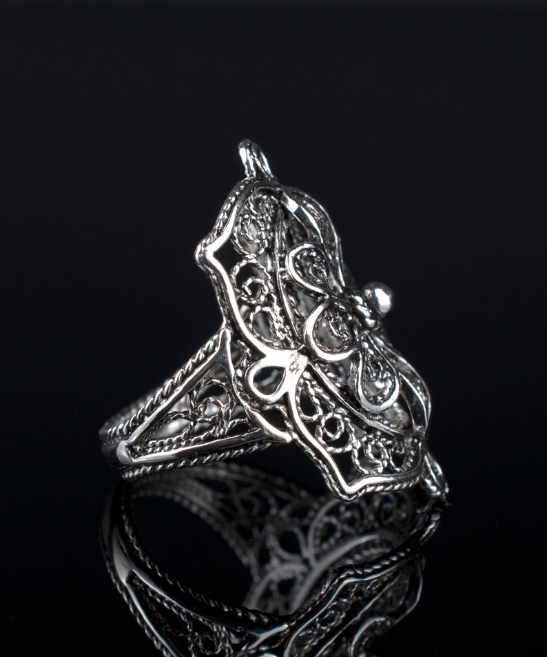 May include: A silver filigree ring with a delicate butterfly design. The ring is made of intricate, openwork metal and has a smooth, polished finish.