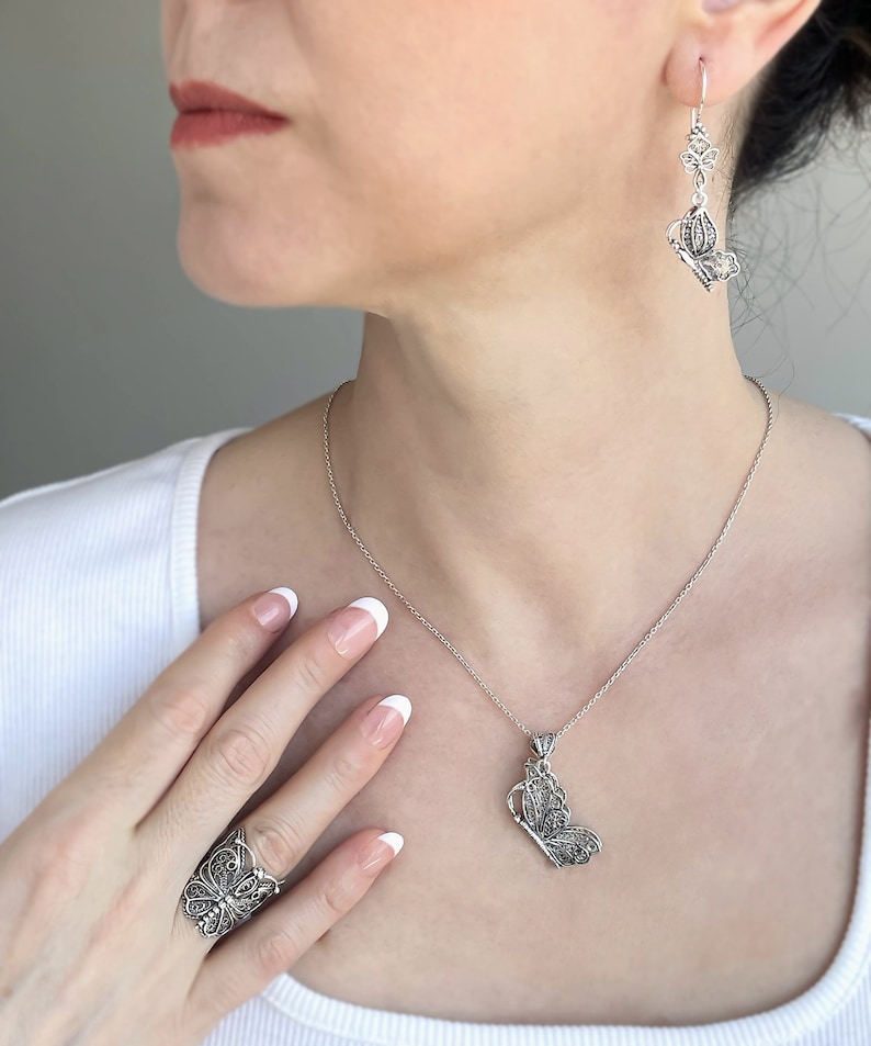May include: A silver necklace and earrings set featuring a delicate butterfly design. The necklace has a pendant with a detailed butterfly charm, while the earrings are dangle style with a smaller butterfly charm.