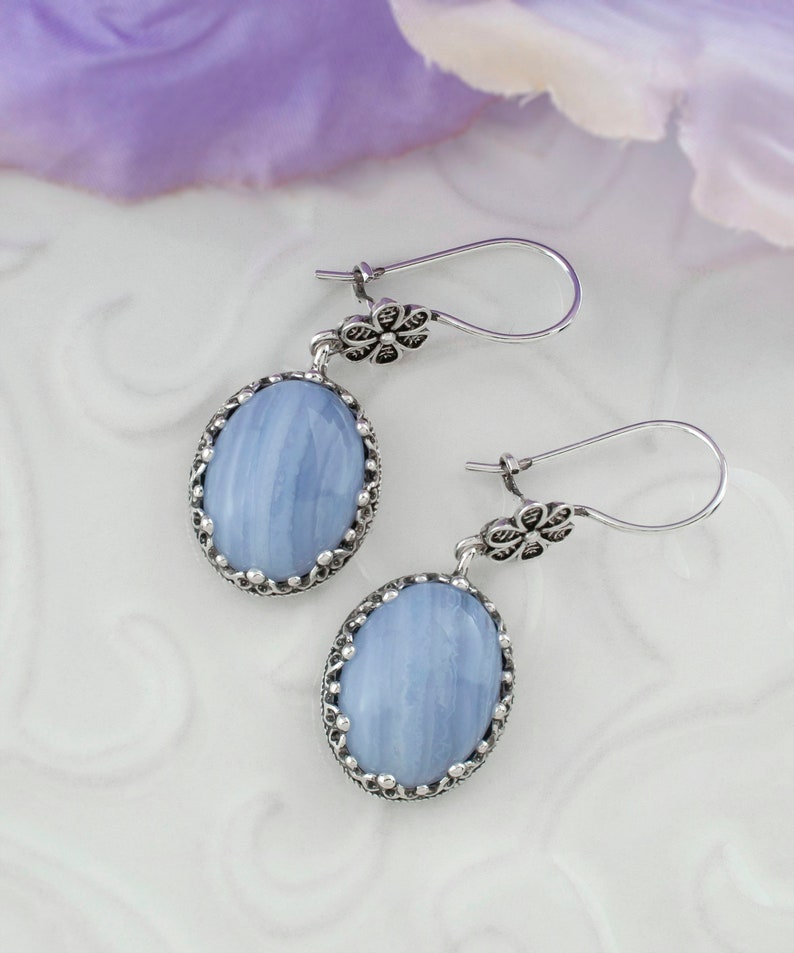 May include: A pair of silver earrings with blue agate stones set in a filigree design. The stones have a light blue color with white streaks.