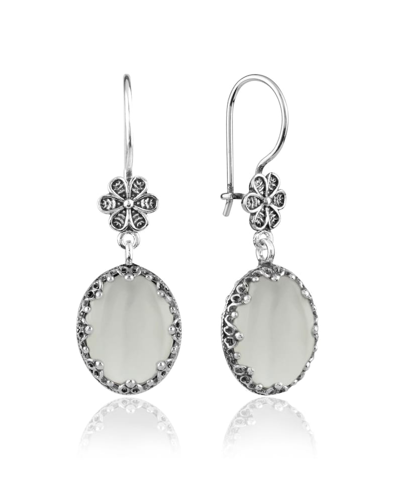May include: A pair of silver dangle earrings with a white oval stone and a floral design.