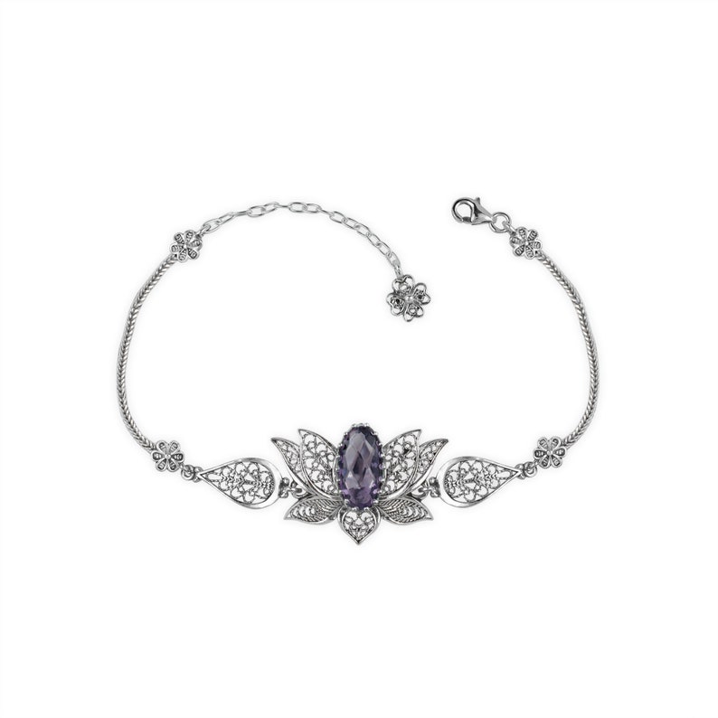 May include: A silver bracelet with a filigree design featuring a purple gemstone in the center. The bracelet is shaped like a lotus flower.