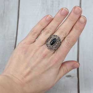 May include: A silver ring with a black oval gemstone set in a filigree design.