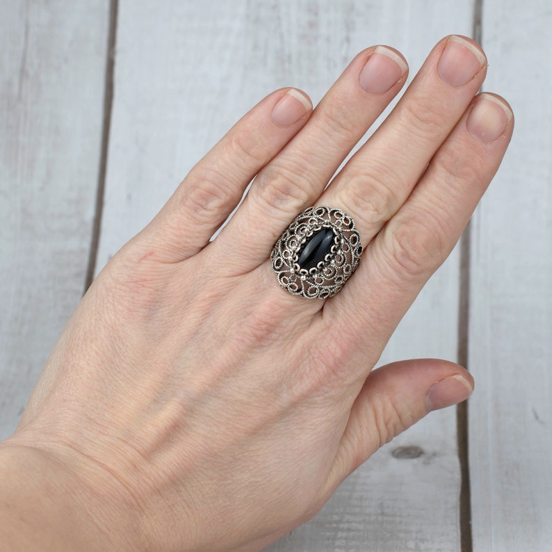May include: A silver ring with a black oval gemstone set in a filigree design.