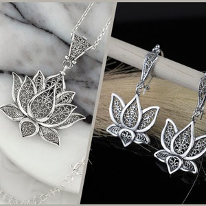 May include: Silver filigree lotus flower necklace and earrings. The necklace has a delicate chain and the earrings are drop style.