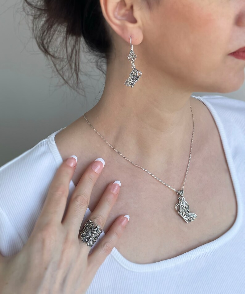 May include: A silver butterfly necklace, ring, and earrings set. The necklace features a delicate butterfly pendant, while the ring and earrings have more intricate designs.