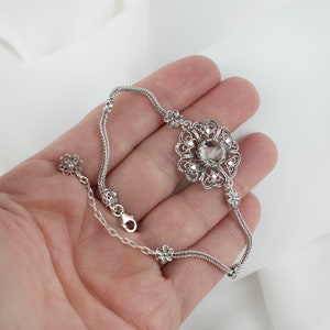 May include: A silver bracelet with a delicate chain and a large, ornate flower pendant featuring a clear gemstone in the center.