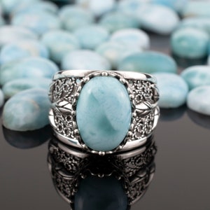 May include: A silver ring featuring a large oval blue gemstone set in a filigree design. The ring is surrounded by smaller blue gemstones.