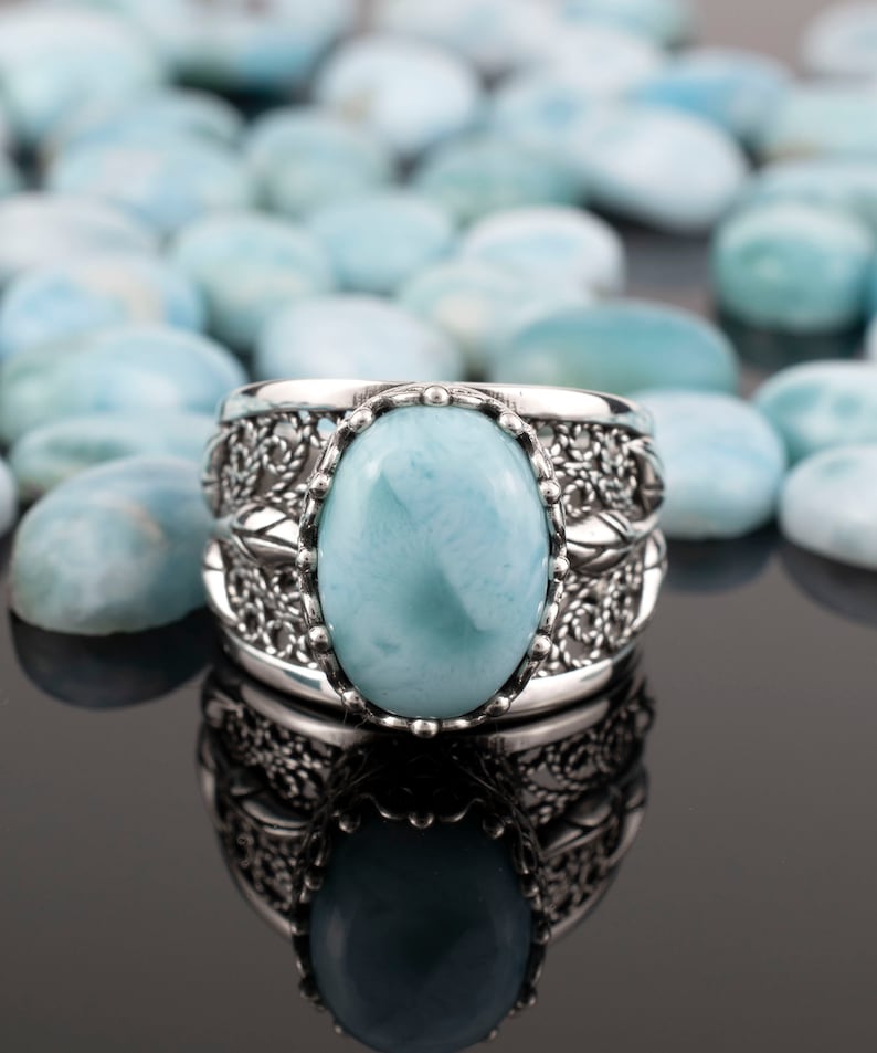 May include: A silver ring featuring a large oval blue gemstone set in a filigree design. The ring is surrounded by smaller blue gemstones.
