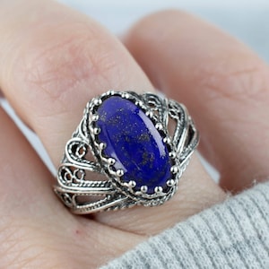 May include: A silver ring featuring an oval lapis lazuli gemstone set in a filigree design.