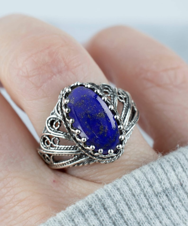 May include: A silver ring featuring an oval lapis lazuli gemstone set in a filigree design.