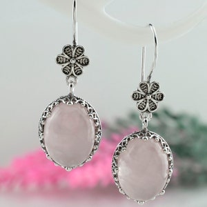 May include: A pair of silver earrings with a pink rose quartz stone and a floral design.