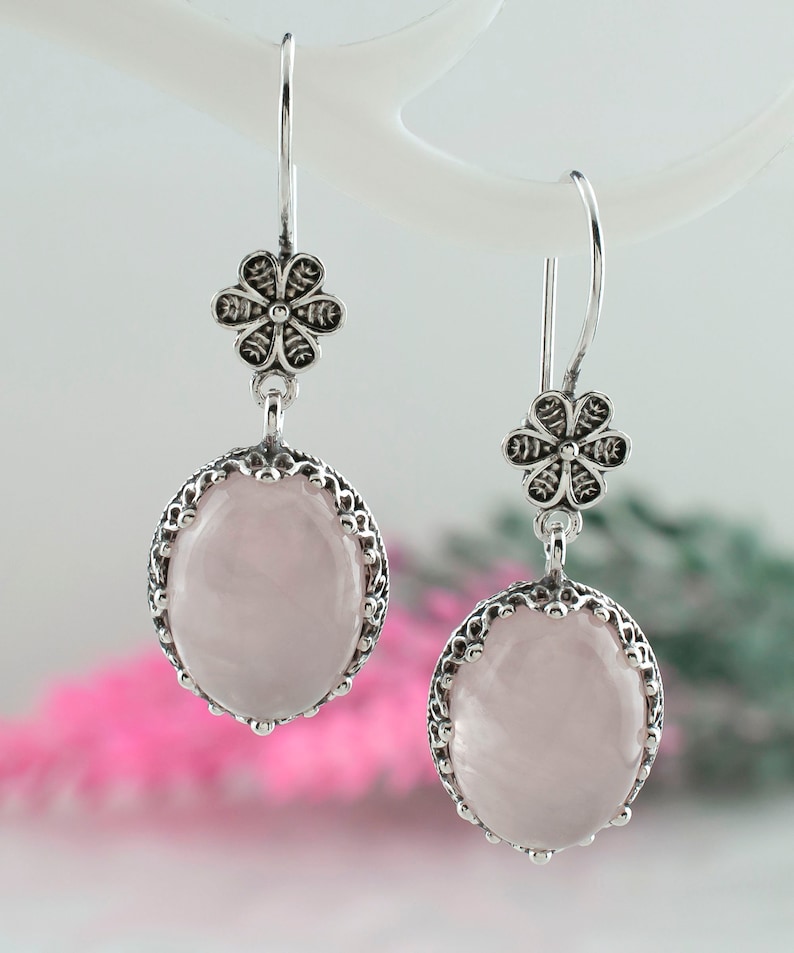 May include: A pair of silver earrings with a pink rose quartz stone and a floral design.