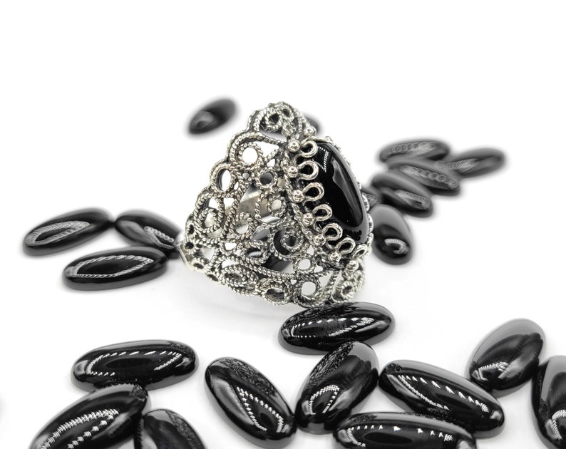 May include: A silver ring with a black oval gemstone set in a filigree design.