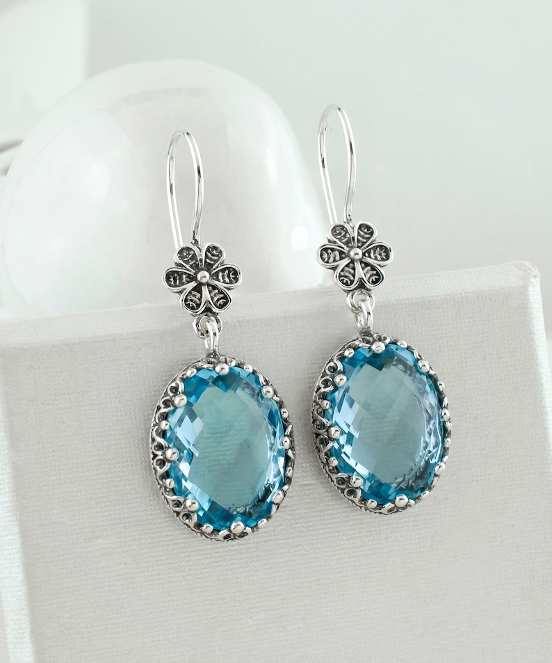 May include: A pair of silver dangle earrings with blue gemstone drops and floral accents.