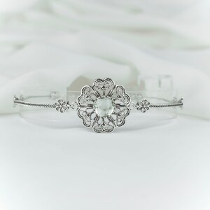 May include: A silver bracelet with a clear crystal in the center of a filigree flower design.
