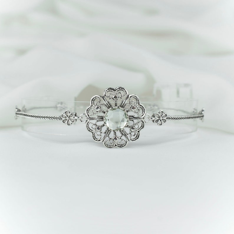 May include: A silver bracelet with a clear crystal in the center of a filigree flower design.