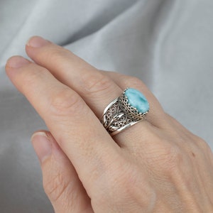 May include: A silver ring featuring a blue and green gemstone set in a filigree design.