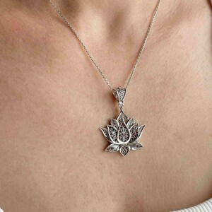 May include: A silver chain necklace with a delicate, filigree lotus flower pendant. The pendant is intricate and detailed, with a floral design.