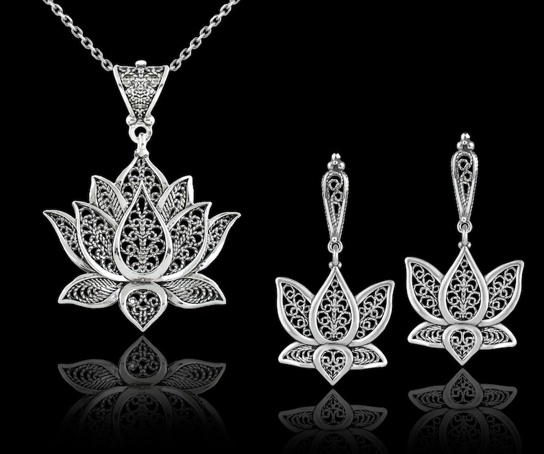 May include: A silver lotus flower pendant necklace and matching earrings. The pendant and earrings are made of intricate filigree work and have a delicate, feminine design.