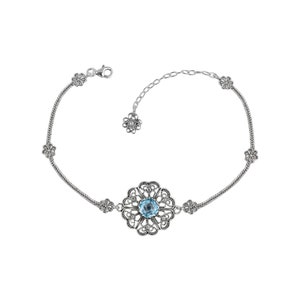 May include: A silver bracelet with a delicate chain and a large, ornate pendant featuring a blue gemstone surrounded by filigree details.
